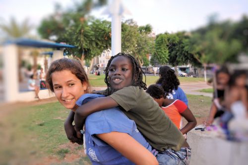 Israel: Children in Israel - Lewinsky Garden, South Tel-Aviv - Volunteer youth movement member giving girl a piggyback ride.